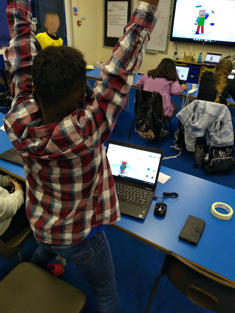 A boy with his arms in the air in front of a computer screen