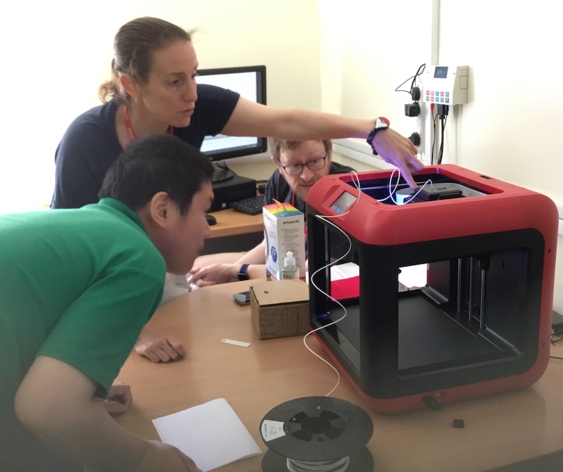 A child looking at a 3D printer, while the teacher points out where the filament is melted